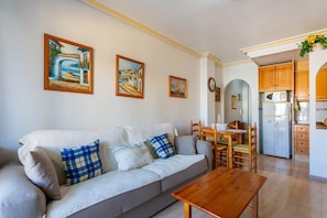 Una sala de estar con sofá, una mesa de madera y una cocina con armarios y electrodomésticos.