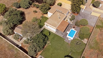 An aerial view of a residential property with a swimming pool, a detached garage, and a well-maintained lawn.
