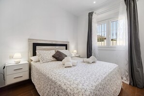 Una cama bien hecha con una colcha estampada, dos lámparas de noche, una mesita de noche y una ventana con cortinas.