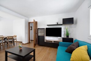 Una sala de estar moderna con una televisión de pantalla plana, un sofá color turquesa, una mesa de centro y un comedor con sillas de madera y una mesa.