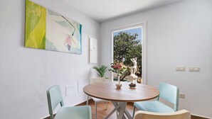 A dining area with a round wooden table, two chairs, a vase with flowers, and a painting on the wall. - Holiday Home La Alberca with Pool, Garden and Wi-Fi (Chiclana de la Frontera)