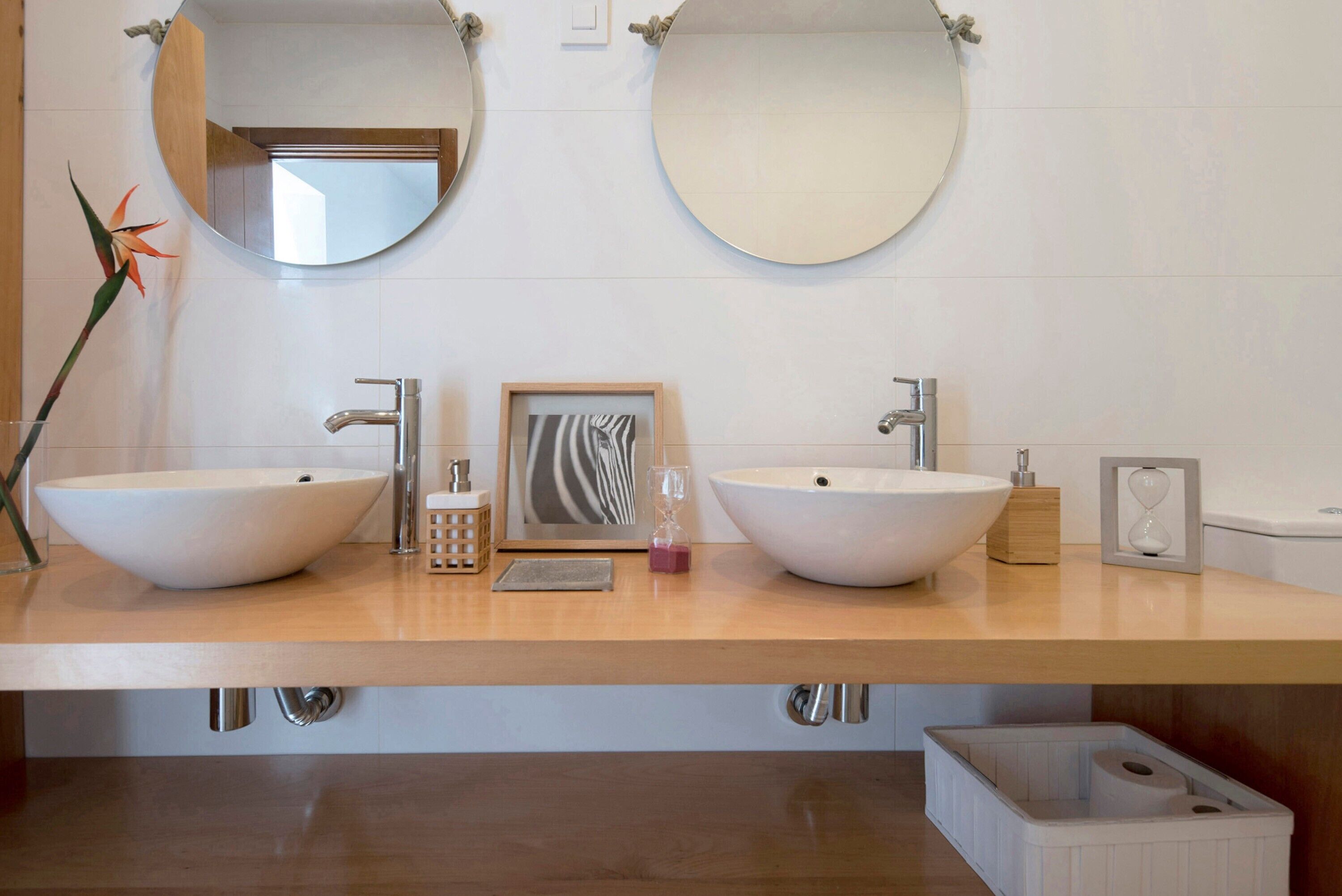 Een badkamer met twee grote ronde spiegels, een houten wastafelmeubel, twee wastafels en een decoratieve plant.