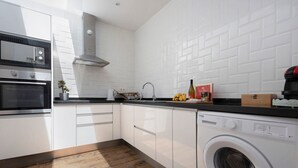 Une cuisine moderne avec des meubles blancs, un four encastré, un lave-linge et une machine à café.