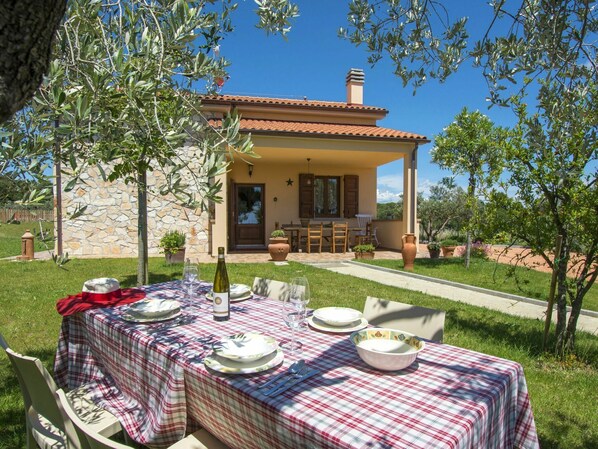 An outdoor dining area with a table set for four, a bottle of wine, and a stone wall in the background.
