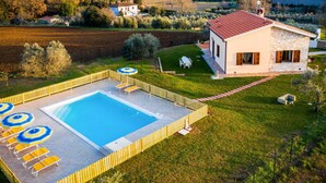 Una casa moderna con piscina, rodeada por un patio cercado y vistas a montañas distantes.