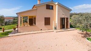 Una casa de dos pisos con un porche cubierto, una chimenea y un camino de entrada de grava.