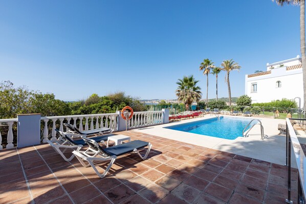 A poolside area with lounge chairs, a swimming pool, and a white building with a balcony.