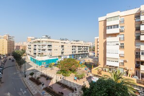 A multi-story building with balconies, a pedestrian area with trees, and a parking lot.