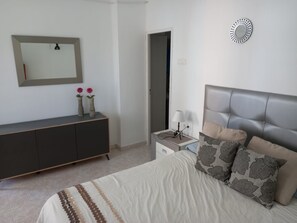 A bedroom with a bed, a dresser, a nightstand, a lamp, and a mirror.