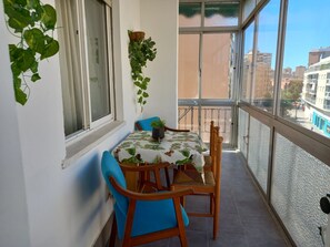 A balcony with a table and chairs, a potted plant, and a view of buildings.