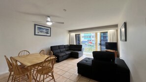 A living room with a dining table, chairs, a black sofa, a television, and a ceiling fan.