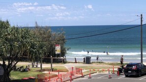 A coastal view with a parking area, a beach with people surfing, and a clear sky.