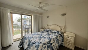 A bedroom with a bed, a nightstand, a ceiling fan, and a view of the outside through a sliding door.