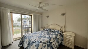 A bedroom with a bed, a nightstand, a ceiling fan, and a view through a sliding glass door.