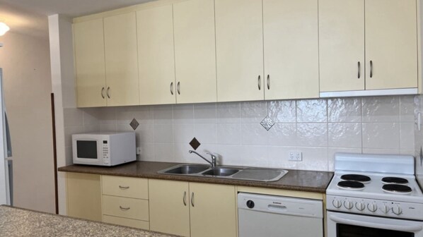 A kitchen with beige cabinets, a microwave, a sink, a dishwasher, and a stove.