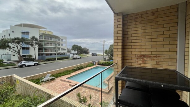 A residential balcony with a pool, a view of a street, and a building in the background.
