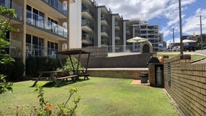 A residential building with multiple balconies, a patio area with a table and chairs, and a brick wall.