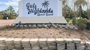 A sign for Gulf Highlands Beach Resort with a palm tree logo, surrounded by a landscaped garden with flowers and a stone wall. - Your Beach Getaway Awaits YOU! (Panama City Beach)