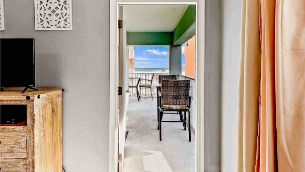 A room with a wooden cabinet, a television, and a view of a balcony with outdoor furniture. - Harbor House 2BR 2BA Gulf-View 1st floor Wrap Balcony Pool King Bed (Gulf Shores)