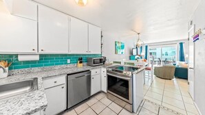 A modern kitchen with white cabinets, a microwave, and a stove. There is a dining area with a table and chairs visible through an open door. - Harbor House 2BR 2BA Gulf-View 1st floor Wrap Balcony Pool King Bed (Gulf Shores)