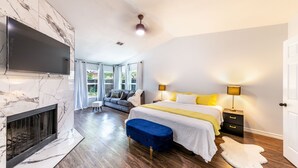 A modern bedroom with a fireplace, a large bed, bedside lamps, and a TV mounted on the wall. - Elite Retreat w/ pool table & shuffleboard @ La Cantera, Six Flags, RIM, UTSA (San Antonio)