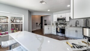 A modern kitchen with white cabinetry, a large island, and stainless steel appliances. - Elite Retreat w/ pool table & shuffleboard @ La Cantera, Six Flags, RIM, UTSA (San Antonio)