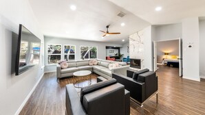 A spacious living room with a sectional sofa, a round coffee table, and a flat-screen TV mounted on the wall. There is a ceiling fan and recessed lighting. - Elite Retreat w/ pool table & shuffleboard @ La Cantera, Six Flags, RIM, UTSA (San Antonio)