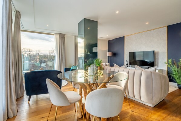 A modern living room with a glass-top dining table, a dark blue sofa, and a beige sectional sofa. - Beautifully Furnished, Central, 2 Bedroom Apartment - With Parking (York)