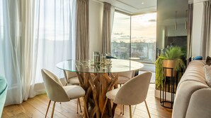 En moderne stue med et spisebord med glasplade, omgivet af stole, en sofa og en potteplante.