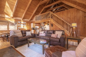 A spacious living room with a high ceiling and wooden beams, furnished with leather sofas and a coffee table.