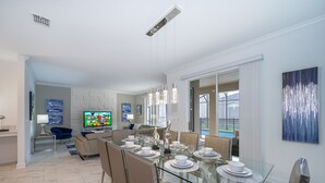 Ett modernt matområde med ett glasbord, metallstolar och en tv-apparat i bakgrunden.