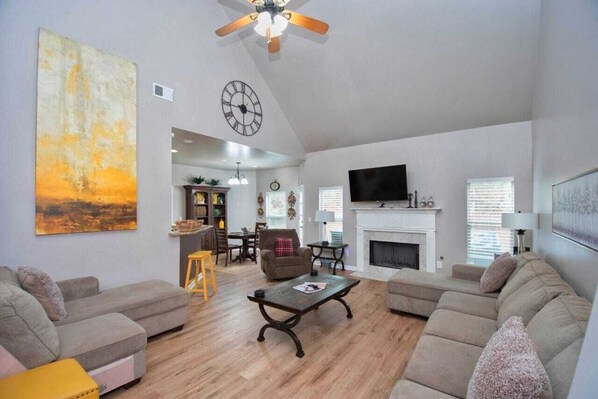 A spacious living room with a fireplace, a television, and a dining area in the background. - 5-Star Luxury Home Sleeps 22+ Airport proximity (Union City)