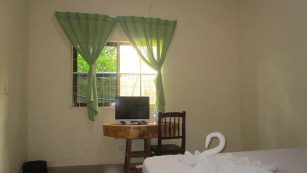 Een kamer met een bed, een bureau met een computer, een stoel en een raam met groene gordijnen.