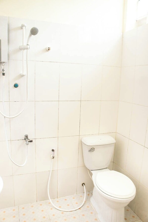 Un baño pequeño y limpio con inodoro, ducha y un dispensador de papel higiénico.