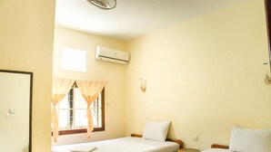 Een kamer met twee eenpersoonsbedden, een raam met gordijnen, een airconditioning en een wandlamp.