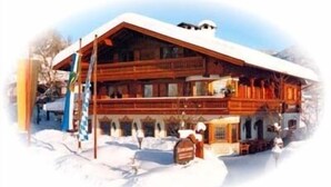 A wooden chalet with a sloped roof, multiple balconies, and a snow-covered ground.