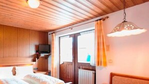 Una habitación con paneles de madera, una cama, una pequeña mesa y un televisor sobre una estantería.