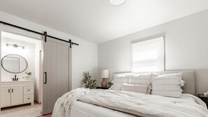 Un dormitorio con cama, mesita de noche, lámpara, cómoda, espejo y puerta corrediza.