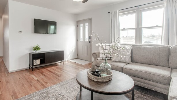 Una sala de estar moderna con un sofá gris, una mesa redonda de centro con objetos decorativos, un televisor de pantalla plana en la pared y un ventilador de techo.