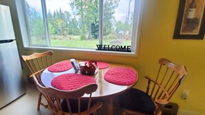 A kitchen with a stainless steel refrigerator, a round table with four chairs, and a window with a 'WELCOME' sign. - Secluded Rural Retreat in the Olympic Foothills Near Olympic National Park (Port Angeles)