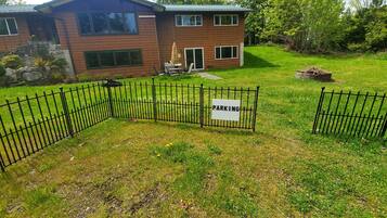 A fenced property with a 'PARKING' sign, a house, and a grassy yard.