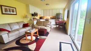 A compact living space with a sofa, a small table, and a kitchen area with cabinets and appliances. - Secluded Rural Retreat in the Olympic Foothills Near Olympic National Park (Port Angeles)