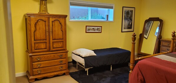 Un dormitorio con un aparador de madera, una cama individual, una ventana con vistas a zonas verdes y un espejo.