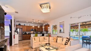 A spacious living area with a modern kitchen, a comfortable seating area, and a view of the outdoor pool. - 5 Mins to beach; 5BD, 4.5BA, Heated pool, Jacuzzi, Mini Golf, Tiki Huts.  (Boynton Beach)