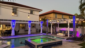 A pool area with a hot tub, outdoor seating, and string lights. - 5 Mins to beach; 5BD, 4.5BA, Heated pool, Jacuzzi, Mini Golf, Tiki Huts.  (Boynton Beach)
