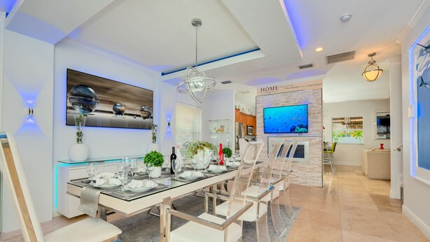 A modern dining room with a glass table, clear chairs, and a chandelier. - 5 Mins to beach; 5BD, 4.5BA, Heated pool, Jacuzzi, Mini Golf, Tiki Huts.  (Boynton Beach)