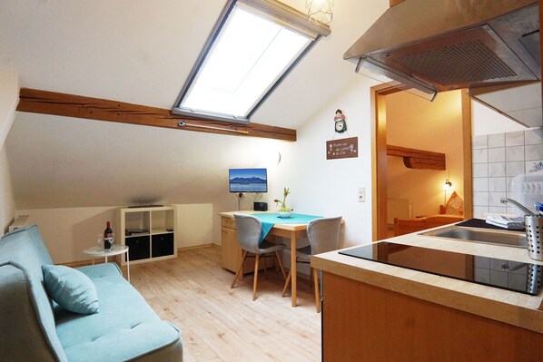 A compact living space with a kitchenette, a dining area, a sofa, and a TV.