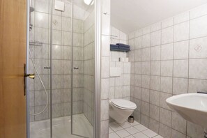 A bathroom with a glass-enclosed shower, a toilet, and a sink.