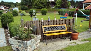 A garden with a wooden bench, a stone planter, and a playground with a slide and swings. - Ferienwohnung III im 2. Stock mit Balkon, Wohnküche, Schlafzimmer, Dusche/wc, Balkon (Chieming)