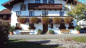 A traditional chalet with a balcony adorned with hanging flower baskets, a wooden bench outside, and a clear sky. - Ferienwohnung III im 2. Stock mit Balkon, Wohnküche, Schlafzimmer, Dusche/wc, Balkon (Chieming)